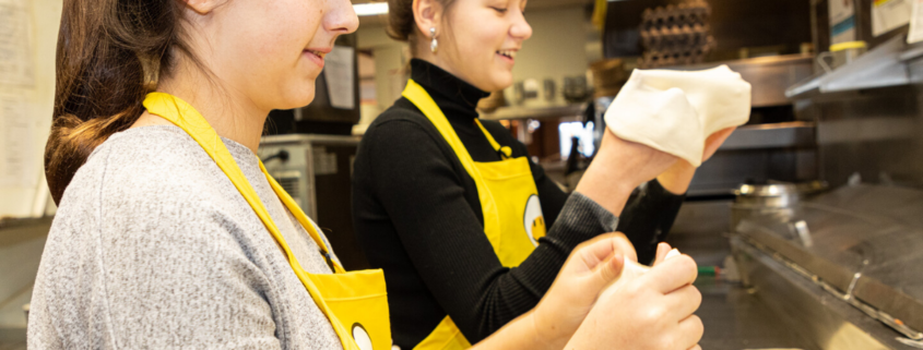 2 young women making pitas in a kitchen