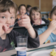 Two kids eating and drinking water with blurred background of other children