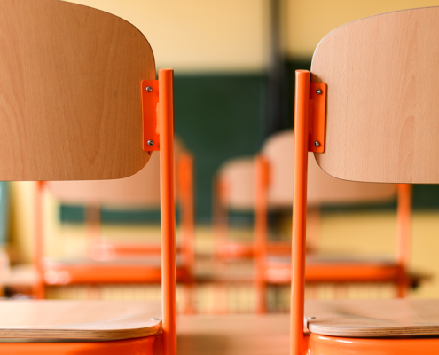 Chairs stacked up on desks with a blurred background of a classroom