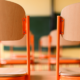 Chairs stacked up on desks with a blurred background of a classroom