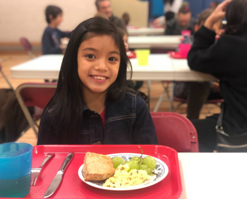 Little girl smiling and enjoying her breakfast of grapes bread and eggs