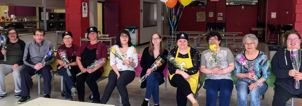 Volunteers sitting in a line with flowers and baloons