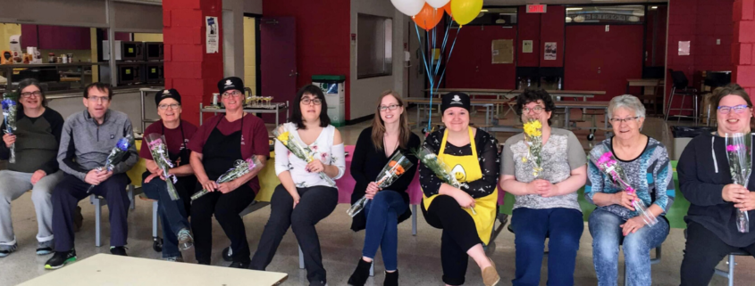 Volunteers sitting in a line with flowers and baloons