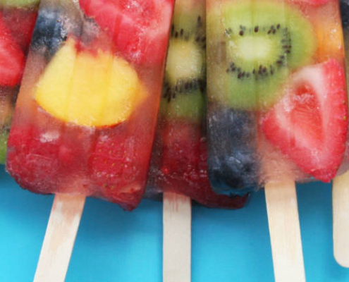 5 fruity popsicles with a mix of fruits in them on a light blue background