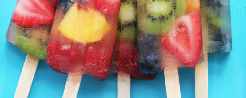 5 fruity popsicles with a mix of fruits in them on a light blue background