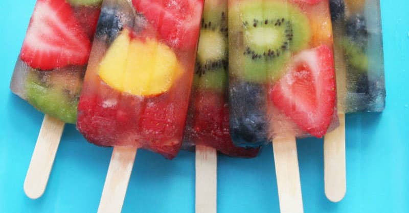 5 fruity popsicles with a mix of fruits in them on a light blue background