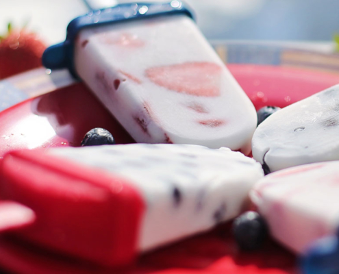 4 berry flavored popsicles on a red plate with blue berries in the middle