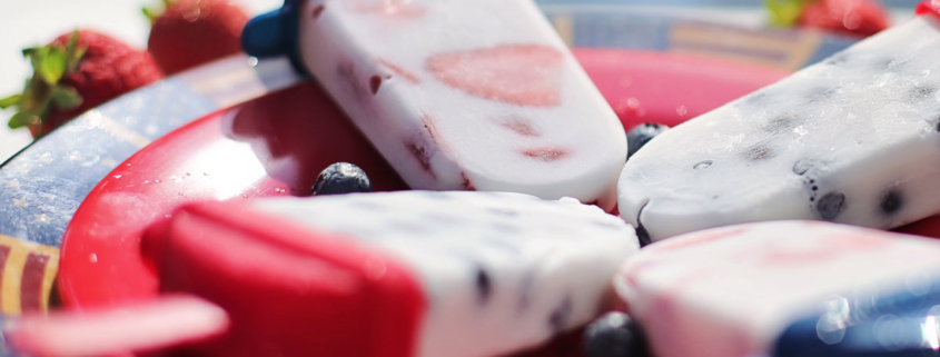 4 berry flavored popsicles on a red plate with blue berries in the middle