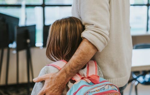 Daughter with a backpack on and father with hand around her