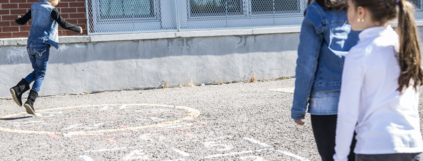 3 children playing hopscotch on a school playground