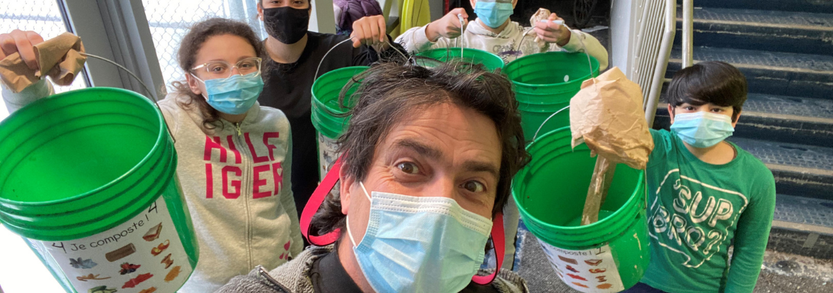 Man and children wearing masks while holding green compost buckets