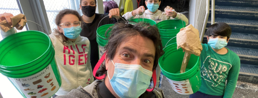 Man and children wearing masks while holding green compost buckets